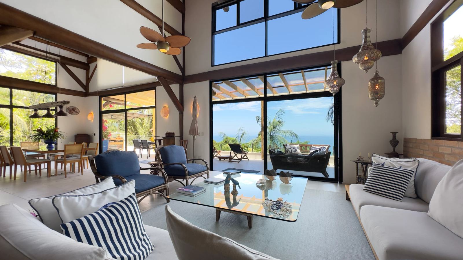 Sala de estar da Villa 231 com pé-direito duplo, grandes janelas e vista para o mar no Condomínio Iporanga.